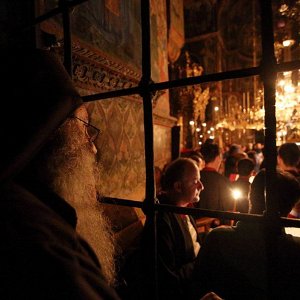 Πιστοί με αναμμένα κεριά μέσα σε εκκλησία σε σκοτεινή ατμόσφαιρα.