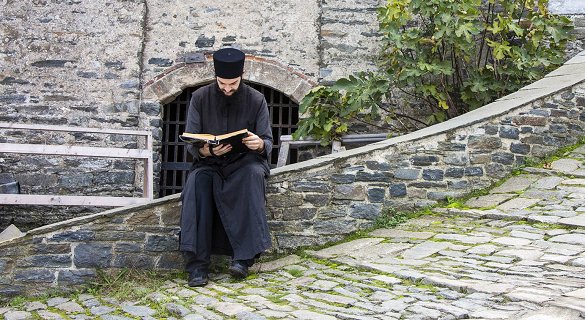 Μοναχός διαβάζει προσευχές σε ένα πέτρινο περβάζι.